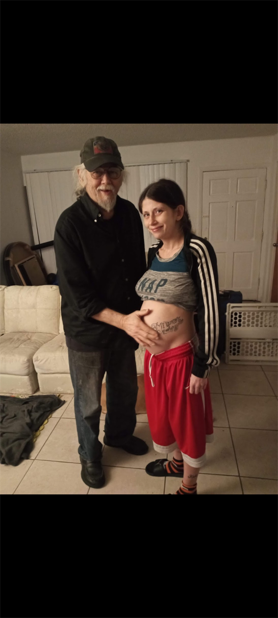 A man and woman share a joyful moment in their living room, celebrating her pregnancy together.