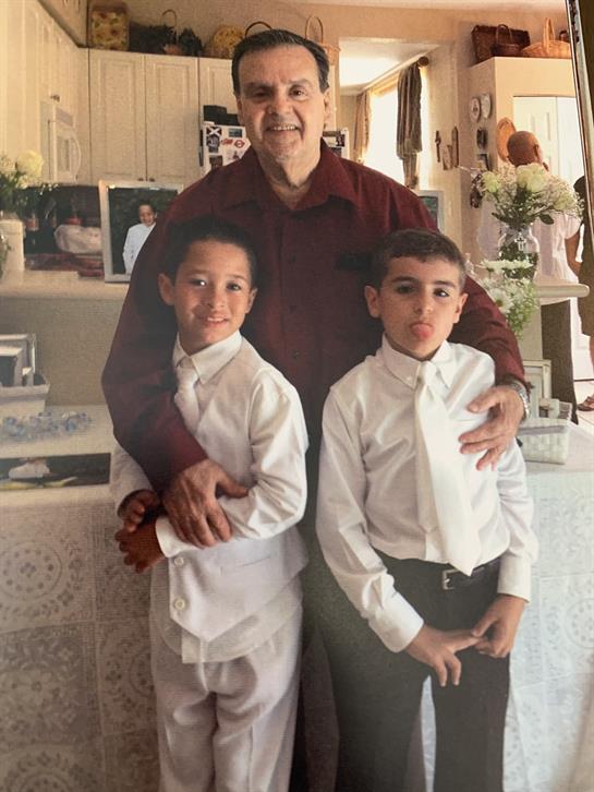 Two boys in white shirts stand with their grandfather at a family celebration.