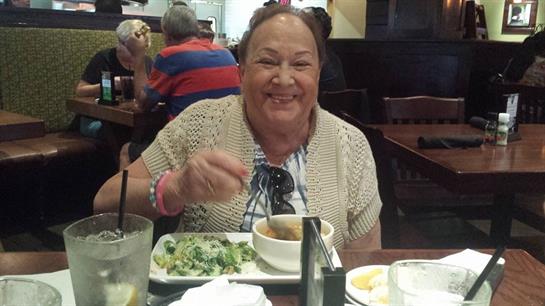 A smiling woman is sharing a meal in a lively restaurant filled with patrons.