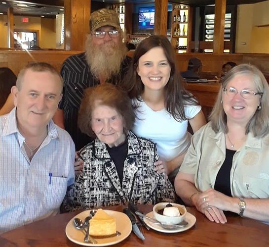 Group of five people smiling together at a restaurant table with dessert in front of them.