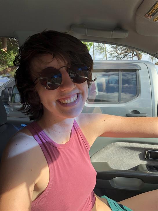 A cheerful woman enjoys the sun while seated in her car, ready for an adventure by the coast.