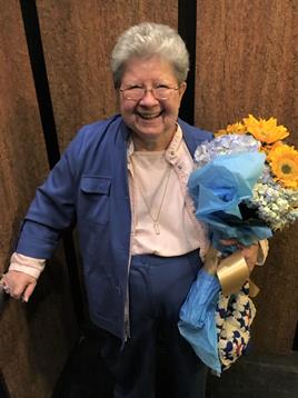 An elderly woman stands in an elevator, joyfully holding a bright bouquet of flowers.
