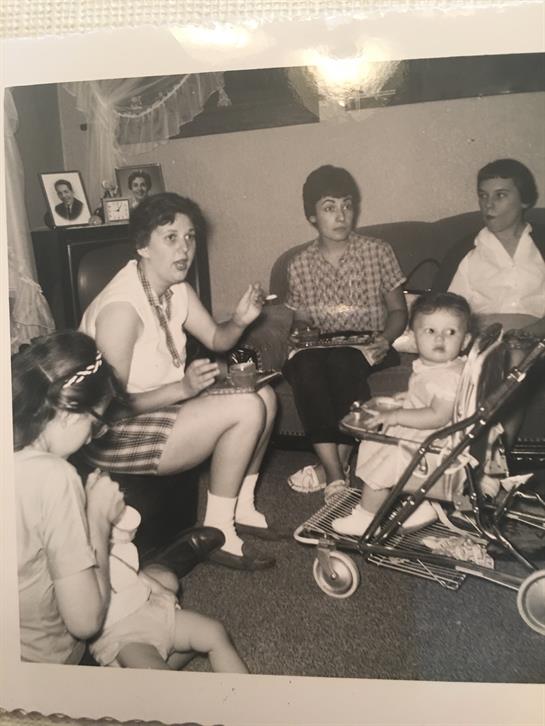 A vibrant family gathering in a cozy living room with adults chatting and a baby in a stroller.
