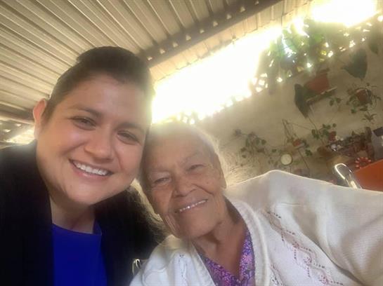 A young woman and an elderly lady joyfully pose together in a warm, bright setting.