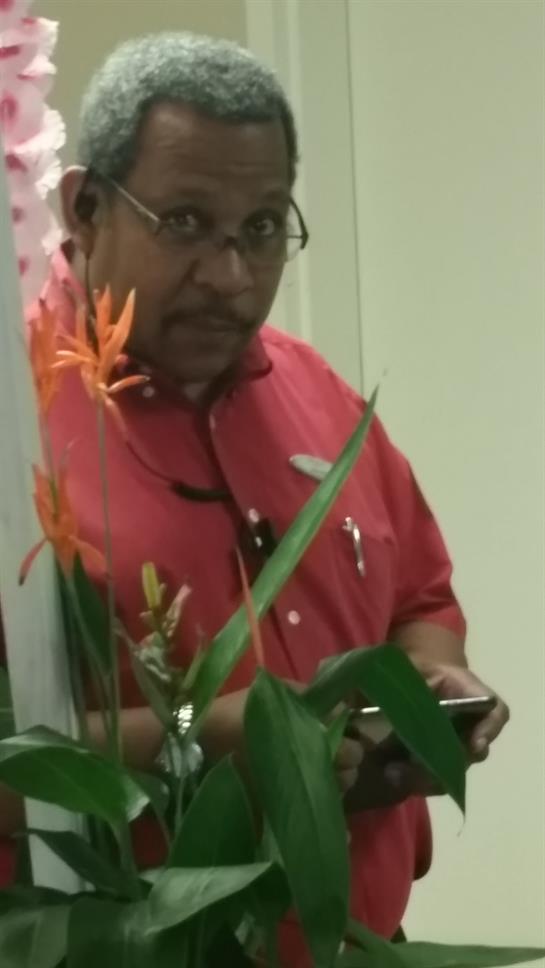 A man in a red shirt admires vibrant flowers while holding a device in a bright indoor space.