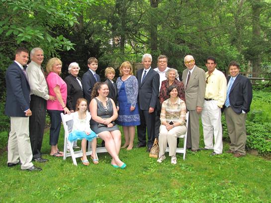 A large family poses together outdoors in a green garden setting, enjoying a joyful reunion.