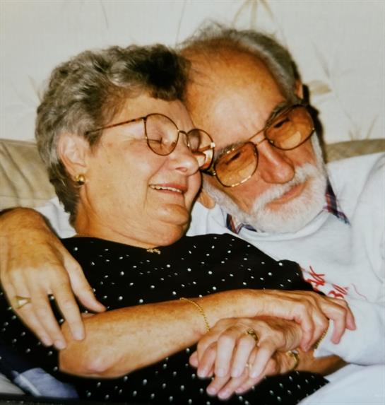 Two elderly individuals share a warm and joyful embrace on a couch, laughing together.