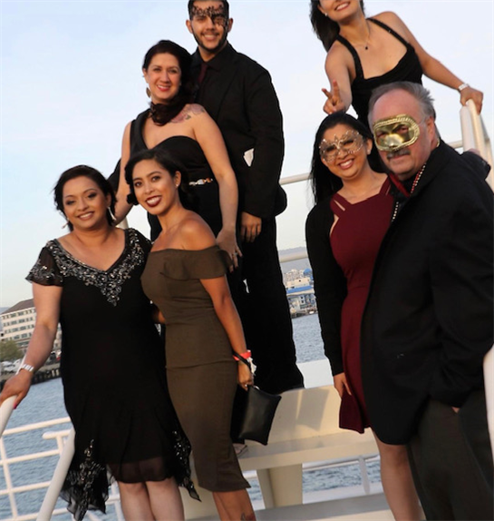 Friends dressed in formal outfits enjoy a festive moment on a boat during sunset along the coast.