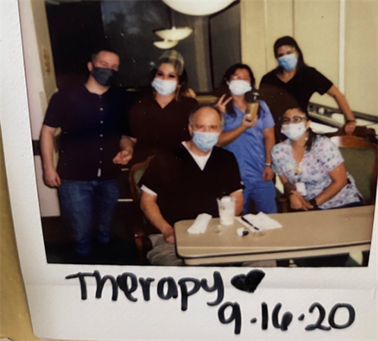 Healthcare professionals and a patient gather during a therapy session while wearing masks.