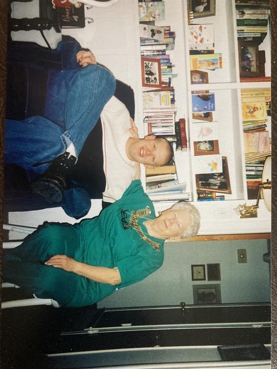 Two people share smiles on a couch in a cozy, book-filled living room.