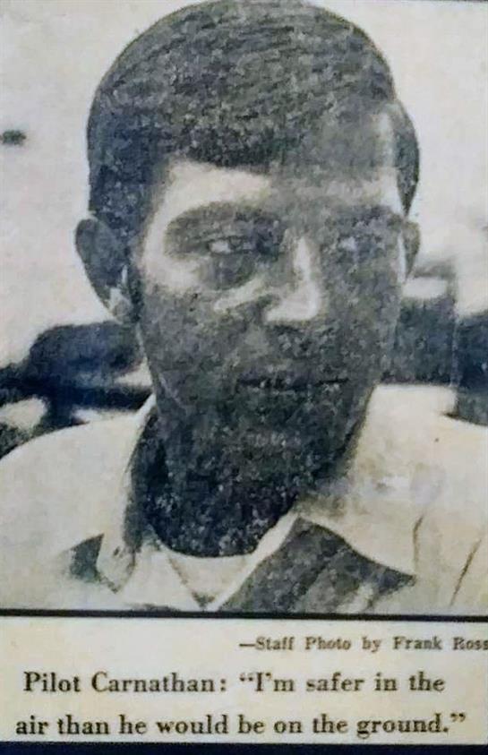 A young man with short hair appears deep in thought while sitting in a busy indoor environment.
