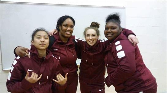 Four athletes in maroon ensembles pose together happily at a gym after practice.