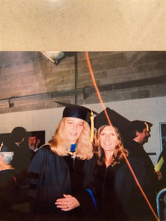Two graduates wearing caps and gowns pose happily at a university celebration event.