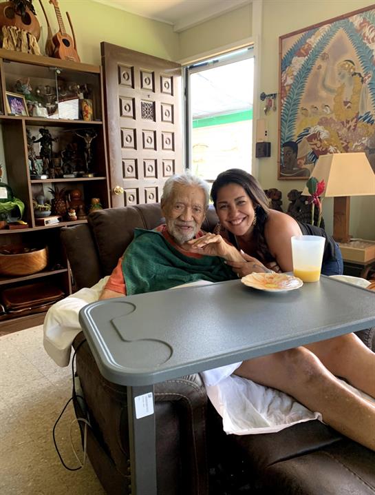 An elderly man shares a happy moment with a young woman in a warm living room filled with memories.