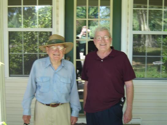 Two men enjoy a friendly moment together on a porch in bright sunlight, showcasing their smiles.