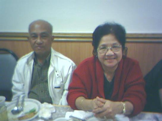 Elderly couple smiles while seated at a table with food items in a warm restaurant atmosphere.
