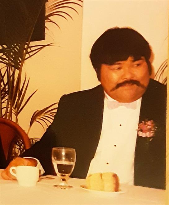 A man in a tuxedo with a thick mustache sits at a table, enjoying a meal during an elegant event.