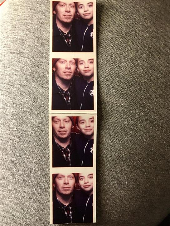 A father and child smile together while taking photos in a photo booth at a fair.