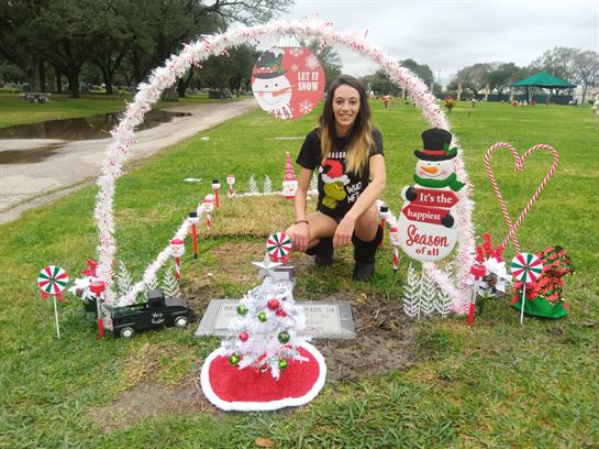 A woman kneels beside a decorated memorial in a park, enhancing it with holiday spirit.