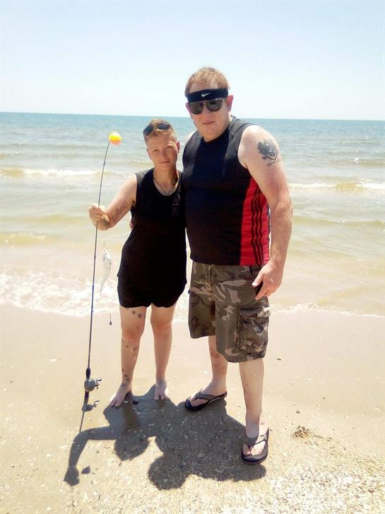 A couple stands on the sandy beach, holding a fishing pole while enjoying the sunny weather.