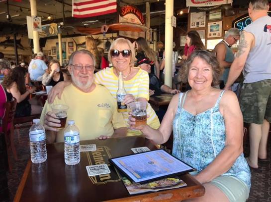 Three friends gather at a bar, sharing drinks and laughter in a vibrant setting with many others.