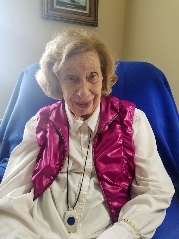 A cheerful elderly woman dressed in a bright vest relaxes in a cozy corner of her home.