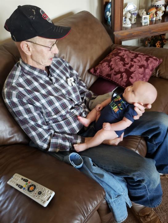 Elderly man lovingly interacts with baby while sitting on a comfortable sofa at home.