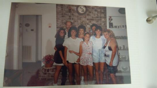 Friends stand together, smiling, in a relaxed living room setting filled with warmth and nostalgia.