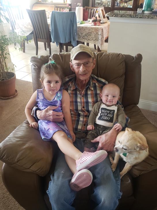Grandfather relaxes in an armchair with two happy grandchildren and a dog, creating joyful memories.