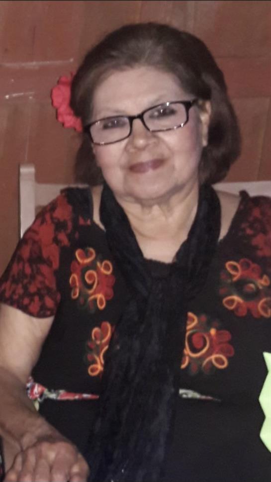 A senior woman wearing a colorful traditional dress and glasses smiles at a cultural event.