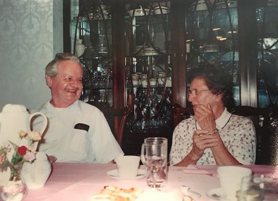 An elderly couple shares laughter and conversation during a family gathering at home.