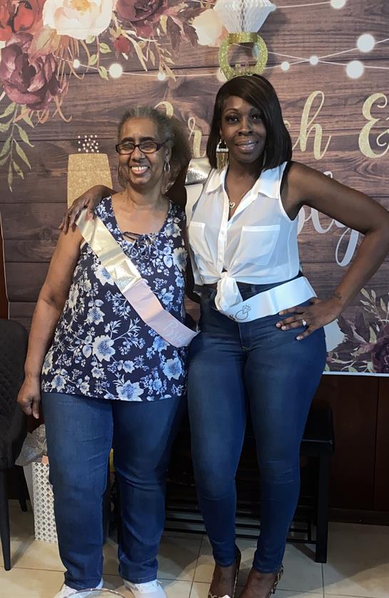 A grandmother and her daughter celebrate together at home, wearing sashes and enjoying the moment.