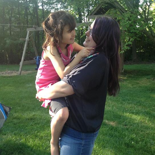 A joyful child nestled in the arms of an adult shares laughter in a green park filled with sunlight.