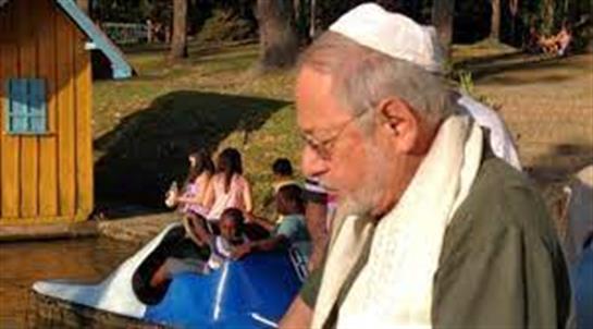 An elderly man with glasses and a kippah enjoys a peaceful moment while families play nearby.