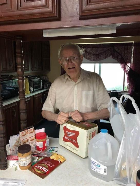 An elderly man stands at a kitchen counter, joyfully preparing snacks with various food items.