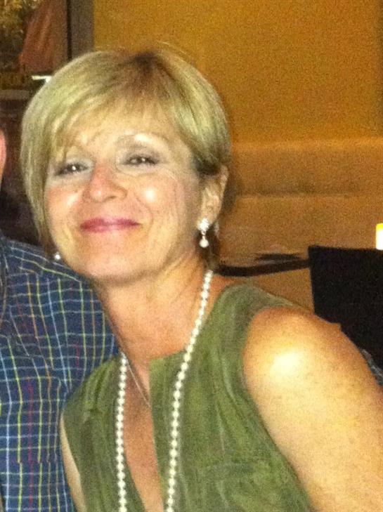 A woman is smiling joyfully during a social gathering in a restaurant with soft lighting.
