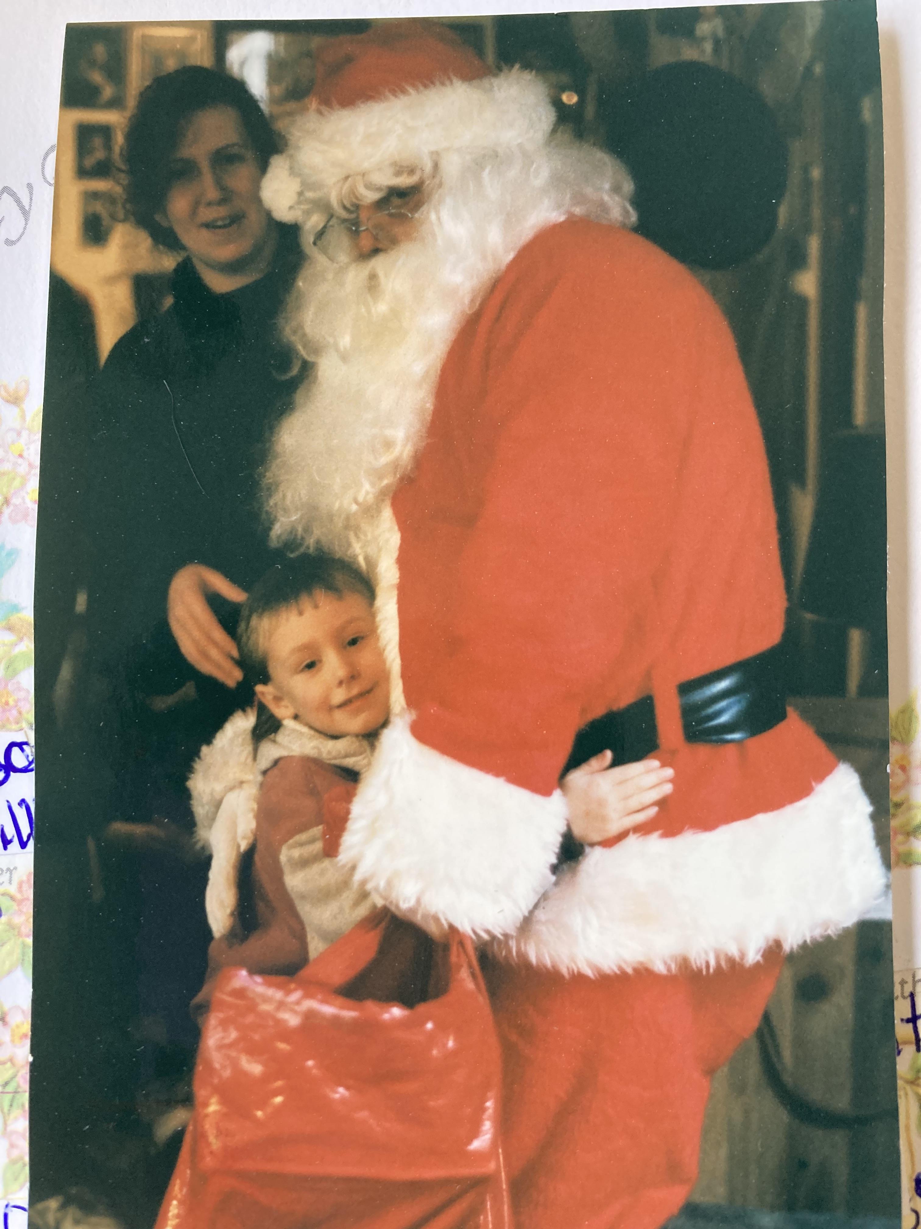 A joyful child hugs Santa Claus while an adult looks on, capturing a moment of holiday cheer.