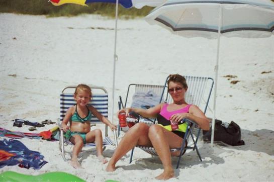 A mother and her child relax on beach chairs while enjoying drinks under bright umbrellas.