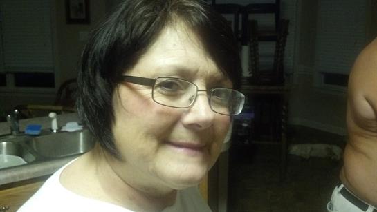 A person with short black hair and glasses smiles, looking relaxed and content.
