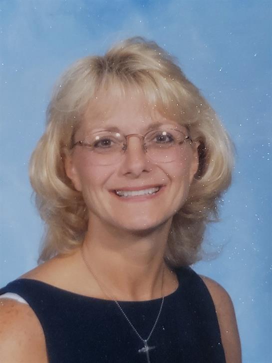 Smiling woman with short blonde hair and glasses poses for a close-up against a light backdrop.