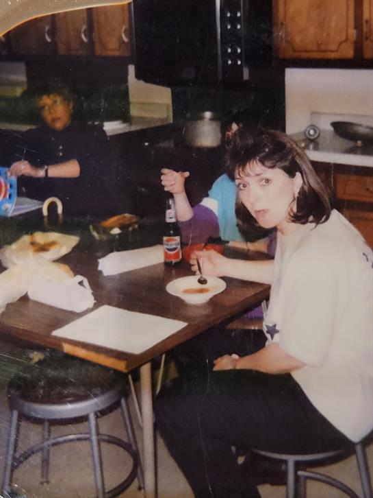 Friends gather around a kitchen table, sharing food and drinks while engaging in conversation.