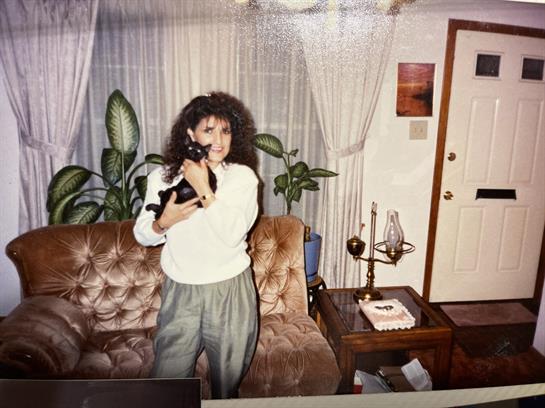 A woman smiles as she embraces her black cat in a welcoming living room filled with plants.