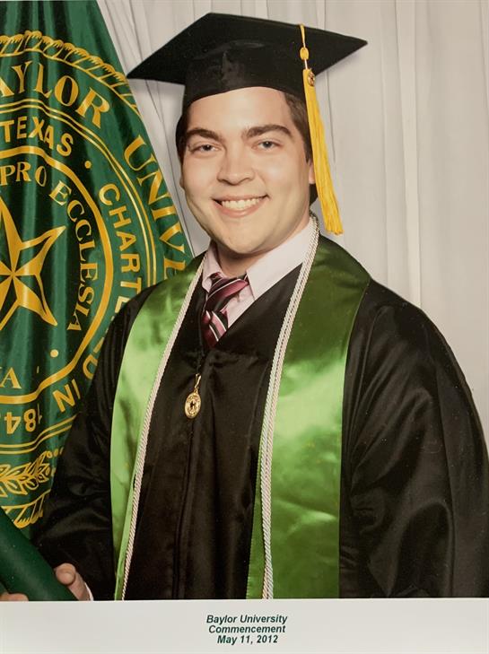 Student in graduation attire smiles with diploma, celebrating academic achievement.