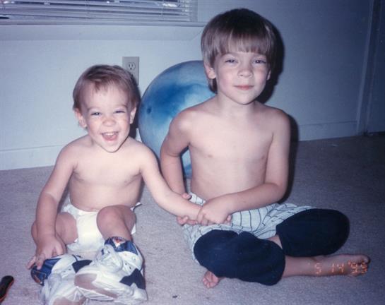 Two boys sit on the floor, laughing and playing happily with toys.