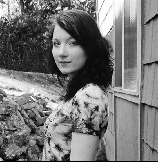 A young woman stands confidently, dressed casually, showcasing her thoughtful gaze outdoors.