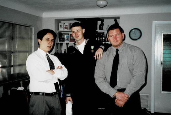 Three well-dressed men stand together, smiling confidently at a social event.
