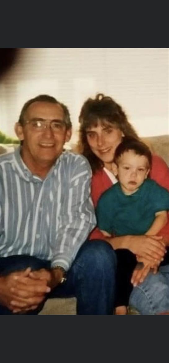A loving family moment shows grandparents with their young grandchild, smiling together on a couch.