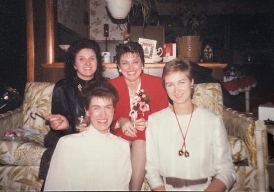 Four women smile together in a living room, enjoying a social event.