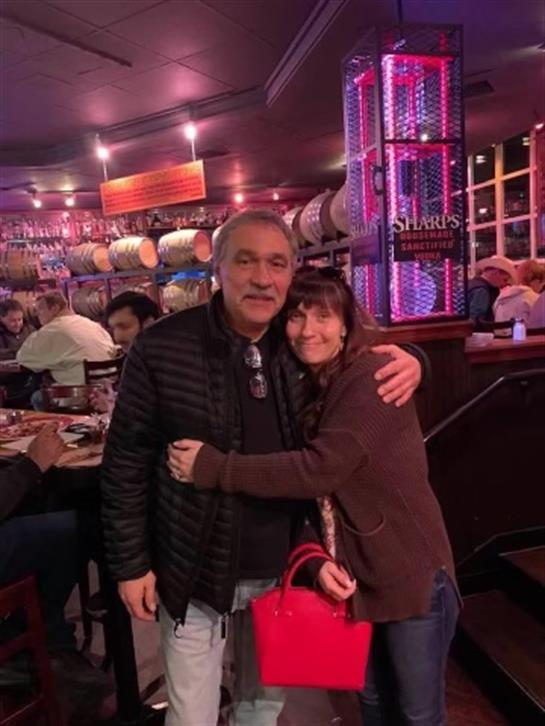 A couple happily embraces in a lively restaurant filled with diners and colorful decor.