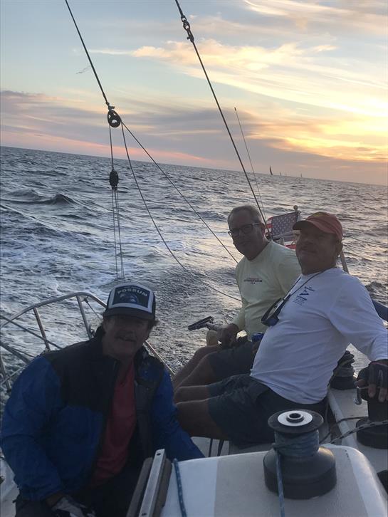 Three friends relax on a sailboat as they navigate the ocean at sunset, enjoying time together.